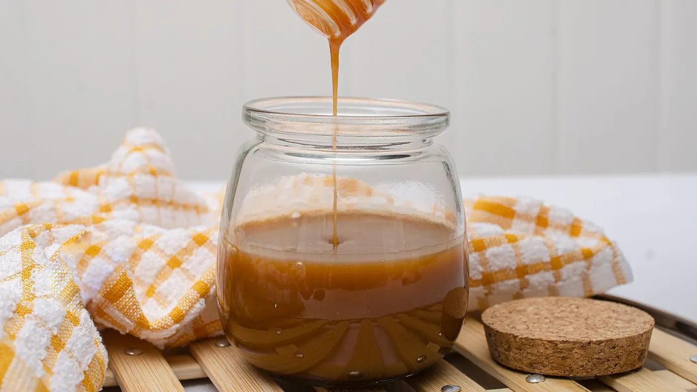 Frasco de vidrio con miel de abejas sobre una superficie de madera